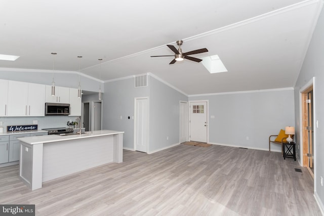 kitchen featuring crown molding, lofted ceiling with skylight, light hardwood / wood-style floors, ceiling fan, and a center island with sink