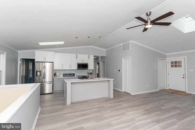 kitchen with lofted ceiling with skylight, pendant lighting, stainless steel appliances, white cabinetry, and light wood-type flooring