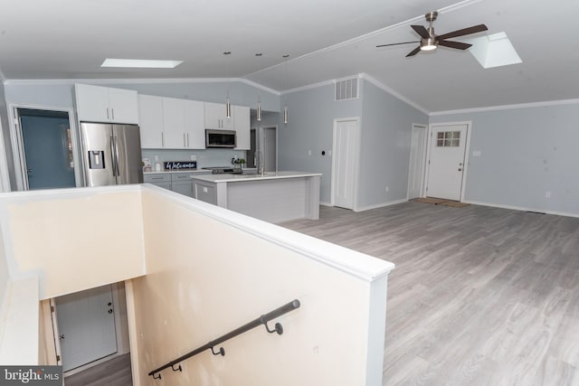 kitchen with vaulted ceiling with skylight, ornamental molding, appliances with stainless steel finishes, and ceiling fan