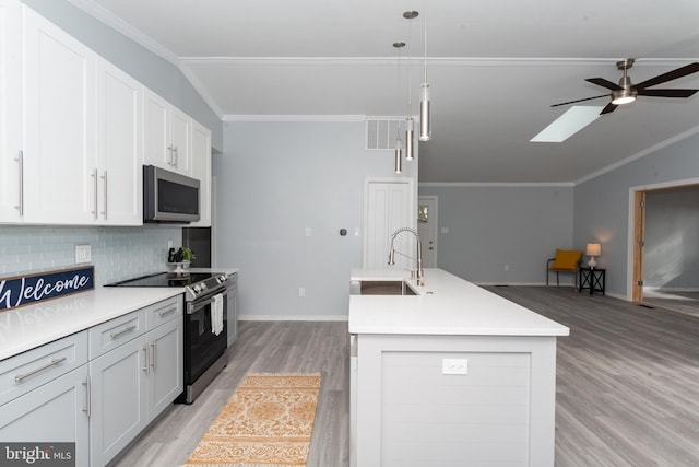 kitchen featuring lofted ceiling with skylight, decorative light fixtures, appliances with stainless steel finishes, sink, and an island with sink