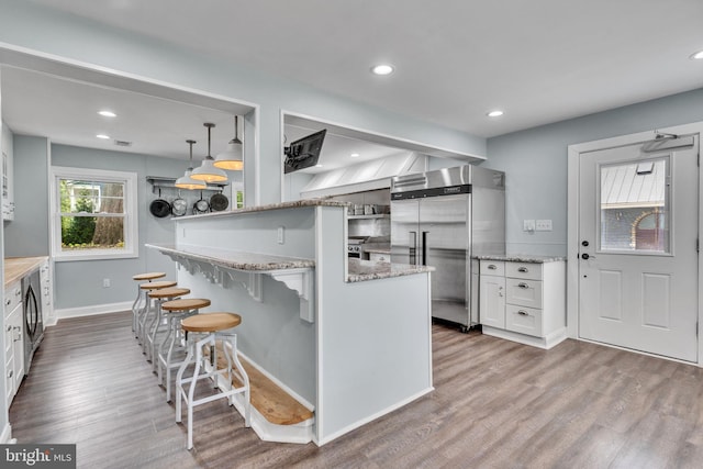 kitchen with white cabinets, built in refrigerator, hanging light fixtures, and hardwood / wood-style floors