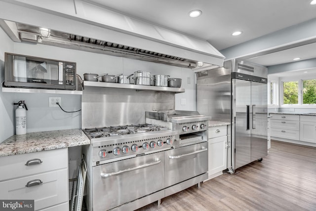 kitchen featuring premium appliances, white cabinetry, light hardwood / wood-style floors, and light stone counters