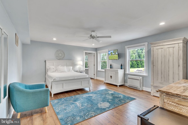 bedroom with heating unit, light hardwood / wood-style floors, and ceiling fan