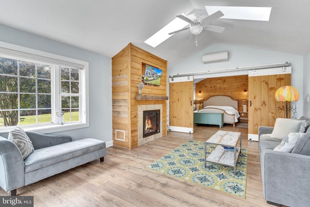 bedroom featuring light wood-type flooring, vaulted ceiling with skylight, a wall unit AC, a tiled fireplace, and ceiling fan