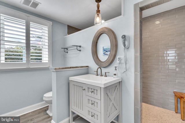 bathroom featuring wood-type flooring, tiled shower, vanity, and toilet