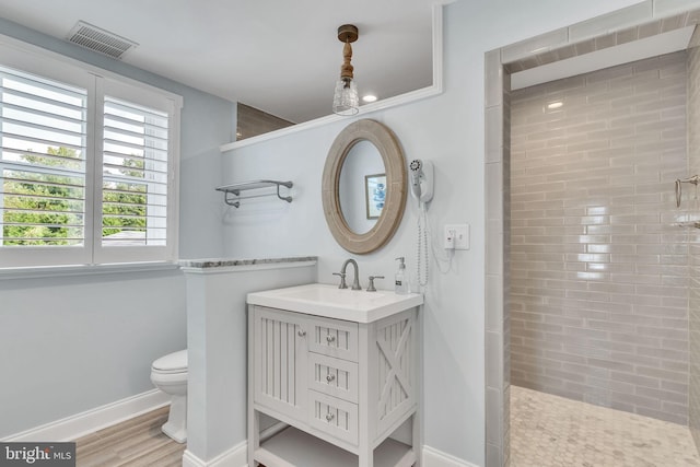 bathroom featuring wood-type flooring, tiled shower, vanity, and toilet