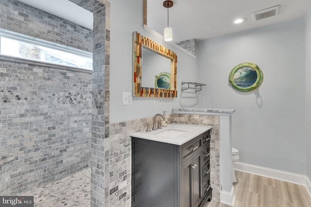 bathroom featuring a tile shower, hardwood / wood-style floors, vanity, and toilet