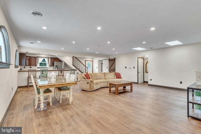 living room with light hardwood / wood-style flooring, a skylight, and a barn door