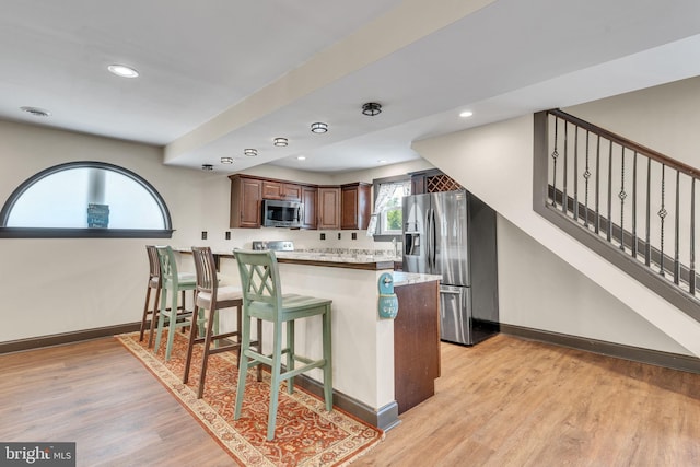 kitchen with stainless steel appliances, kitchen peninsula, light hardwood / wood-style floors, and a kitchen breakfast bar