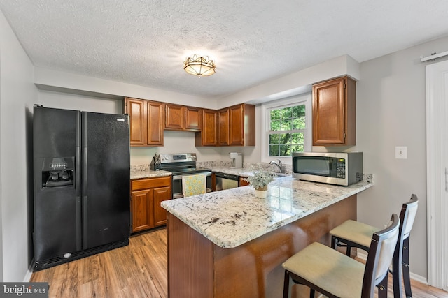 kitchen with light hardwood / wood-style floors, kitchen peninsula, light stone countertops, stainless steel appliances, and a textured ceiling