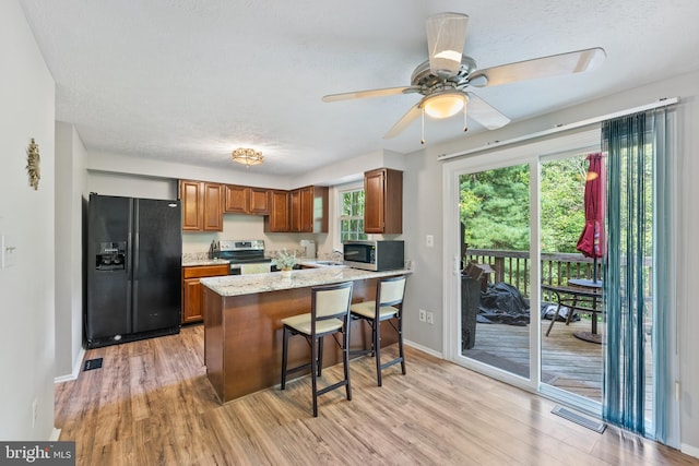 kitchen with light wood-type flooring, light stone counters, a kitchen bar, appliances with stainless steel finishes, and ceiling fan