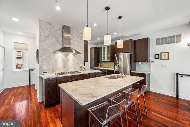 kitchen with wall chimney range hood, appliances with stainless steel finishes, an island with sink, and sink