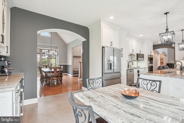 dining space with a notable chandelier, light wood-type flooring, sink, and vaulted ceiling