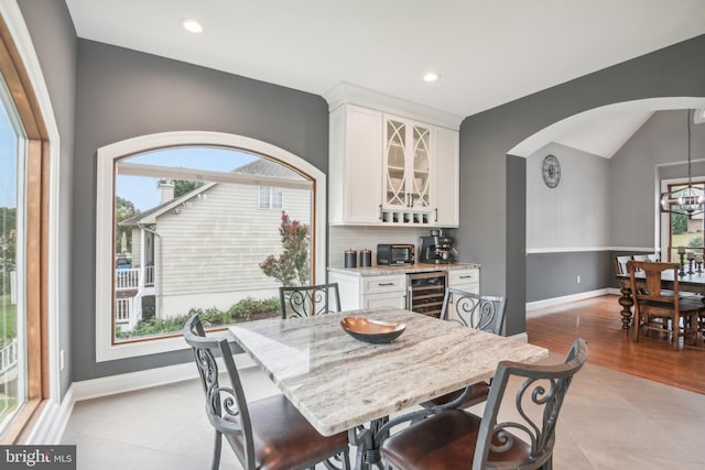 dining area featuring an inviting chandelier, beverage cooler, vaulted ceiling, and light tile patterned floors