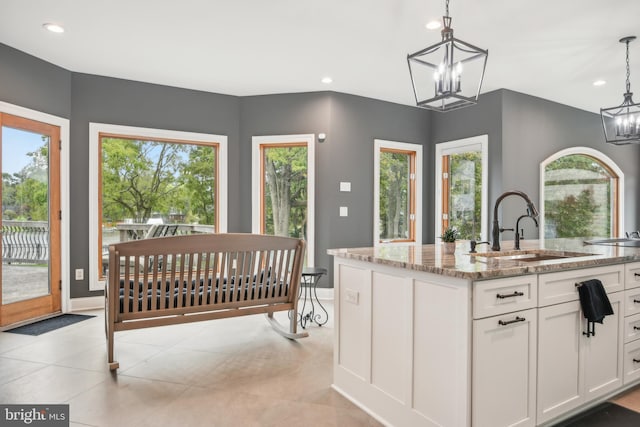 kitchen featuring a center island with sink, white cabinets, light stone counters, and decorative light fixtures