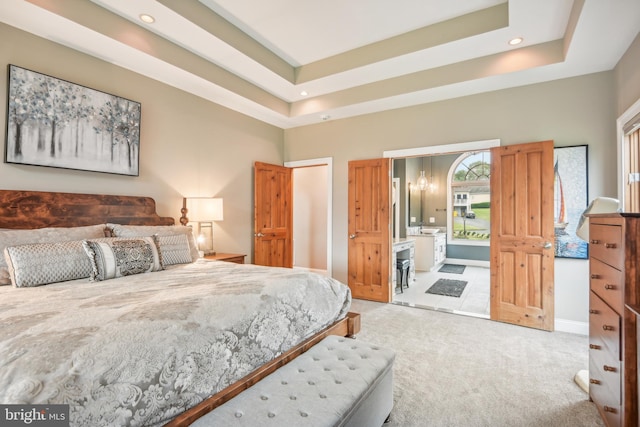 bedroom with light colored carpet, a raised ceiling, and ensuite bathroom