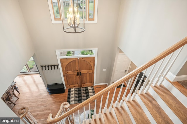 entryway with a notable chandelier, wood-type flooring, and a towering ceiling