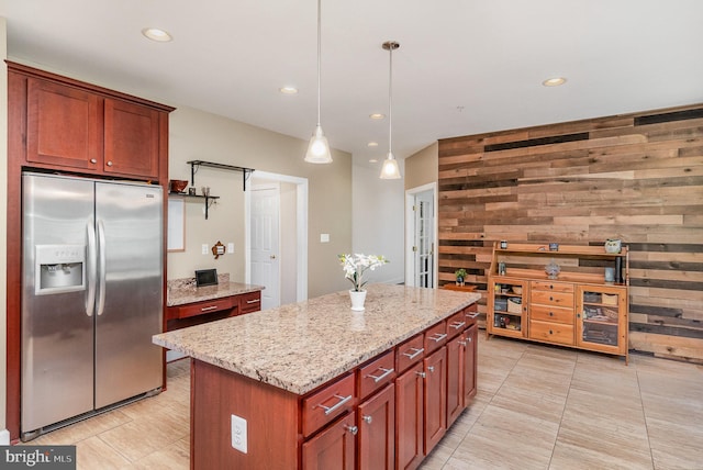 kitchen with a kitchen island, wooden walls, stainless steel fridge, light stone countertops, and decorative light fixtures