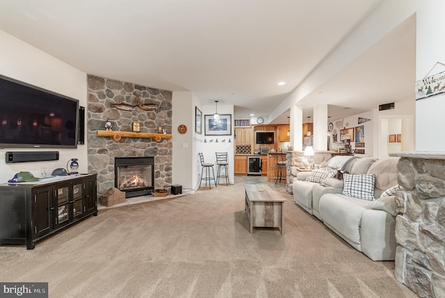 living room featuring light carpet, a stone fireplace, and beverage cooler