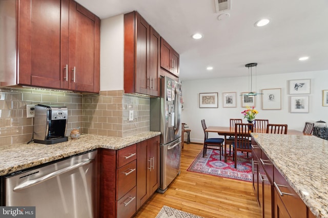 kitchen featuring pendant lighting, light hardwood / wood-style flooring, light stone counters, decorative backsplash, and appliances with stainless steel finishes