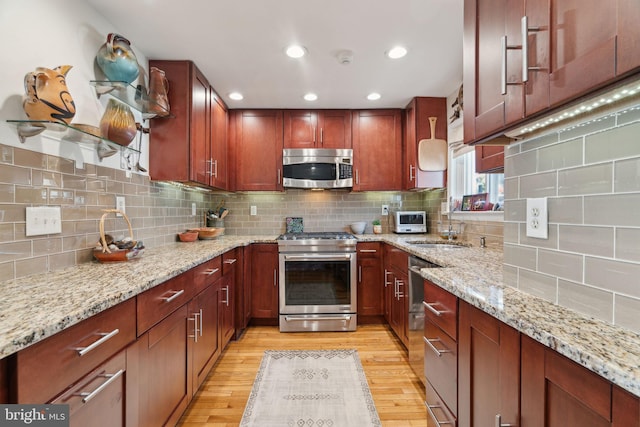 kitchen with light wood-type flooring, light stone counters, stainless steel appliances, and tasteful backsplash