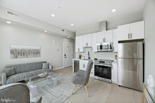 kitchen with appliances with stainless steel finishes, white cabinetry, sink, and light hardwood / wood-style floors