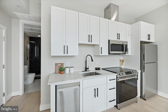 kitchen featuring light wood-type flooring, white cabinetry, light stone counters, sink, and appliances with stainless steel finishes