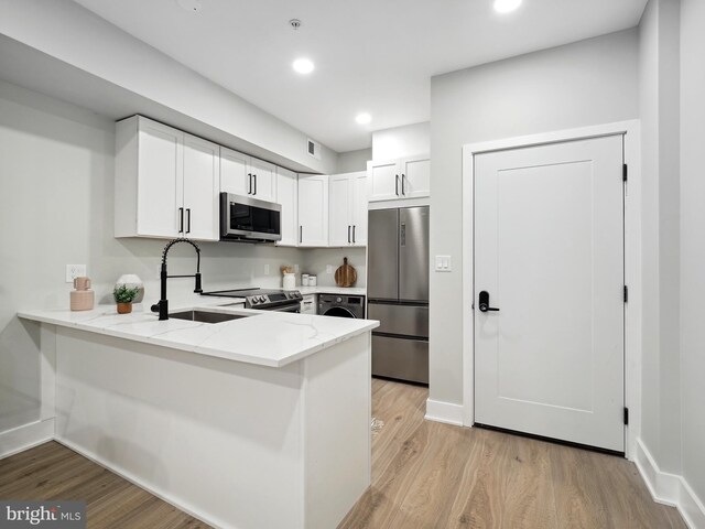 kitchen with light wood-type flooring, sink, appliances with stainless steel finishes, and white cabinetry