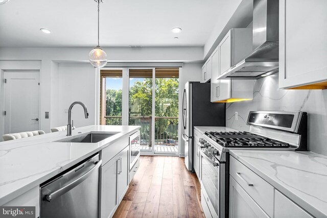 kitchen with a kitchen island with sink, appliances with stainless steel finishes, wall chimney range hood, and light hardwood / wood-style flooring