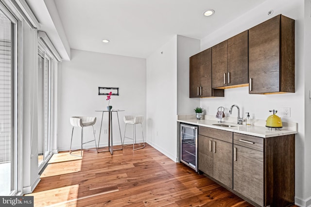 bar featuring dark brown cabinetry, beverage cooler, dark wood-type flooring, and sink