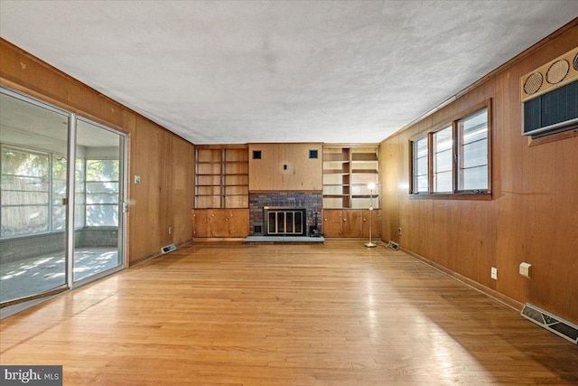 unfurnished living room with wood walls, built in shelves, a fireplace, a textured ceiling, and light hardwood / wood-style floors