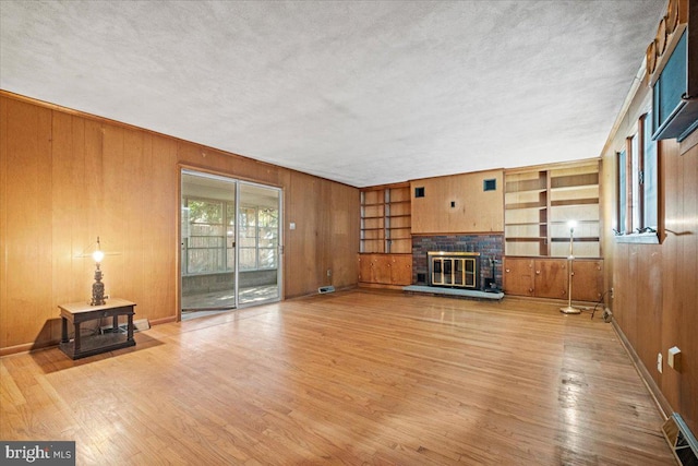 living room featuring a textured ceiling, light wood-type flooring, a fireplace, and wooden walls