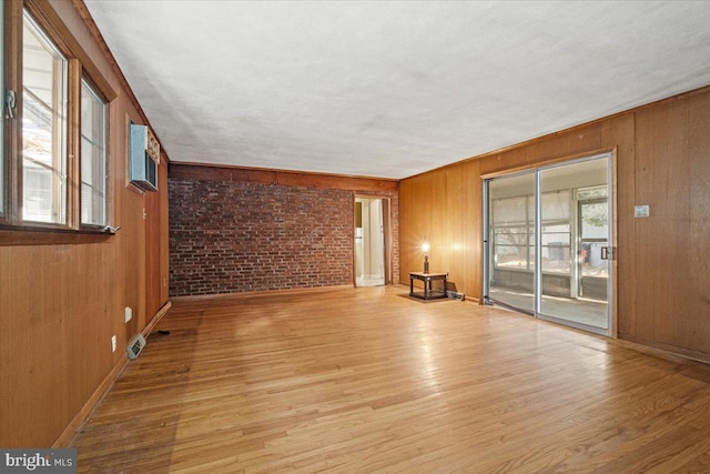 unfurnished living room featuring light wood-type flooring, wooden walls, and brick wall