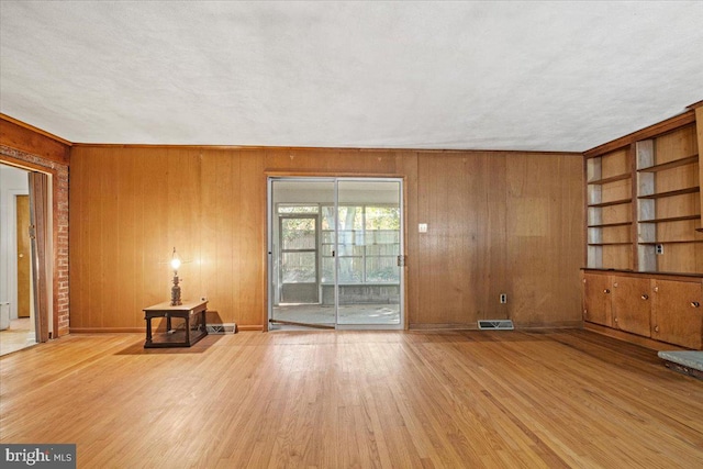 unfurnished living room featuring built in features, a textured ceiling, light hardwood / wood-style flooring, and wooden walls