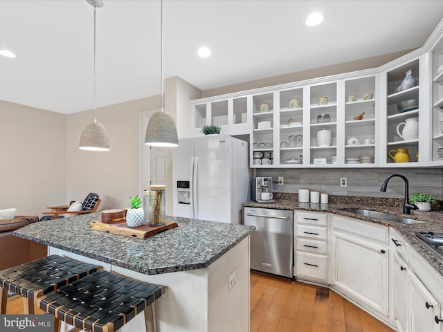 kitchen with dishwasher, white refrigerator with ice dispenser, a breakfast bar area, sink, and decorative light fixtures