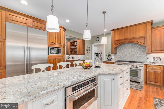 kitchen featuring a breakfast bar, light wood-type flooring, built in appliances, white cabinets, and decorative light fixtures