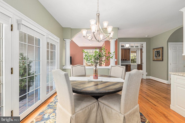 dining room featuring light wood-type flooring, a chandelier, and ornate columns