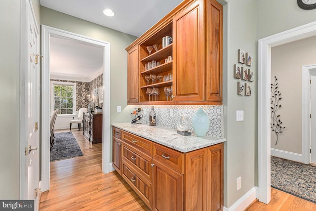 kitchen with light stone countertops, light wood-type flooring, crown molding, and decorative backsplash