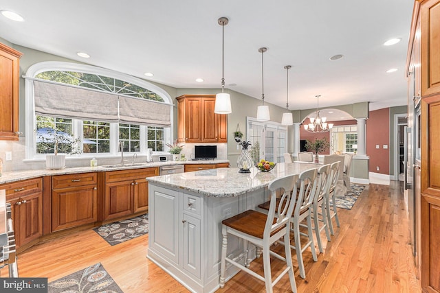 kitchen featuring light wood-type flooring, a chandelier, light stone counters, a breakfast bar area, and a kitchen island