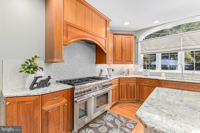 kitchen with light wood-type flooring, light stone counters, tasteful backsplash, sink, and double oven range