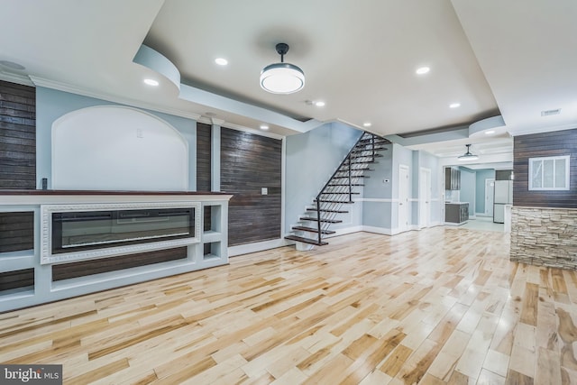 unfurnished living room featuring crown molding, a stone fireplace, and light hardwood / wood-style flooring