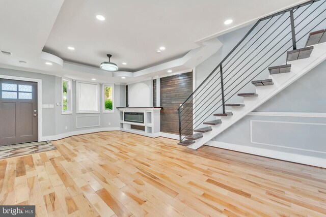 unfurnished living room with ornamental molding, a tray ceiling, and light hardwood / wood-style floors