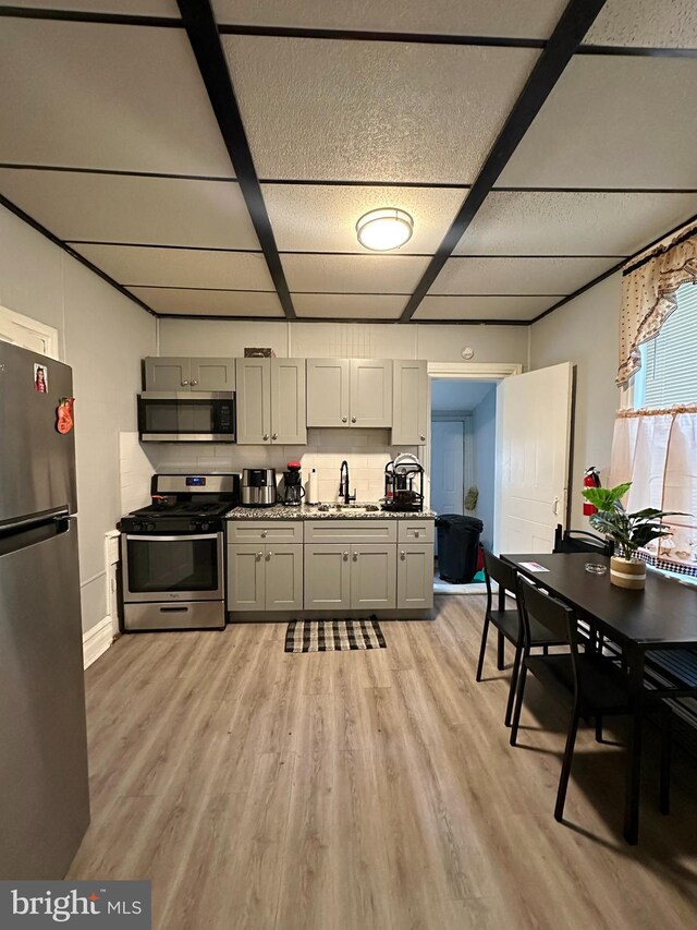 kitchen with light stone counters, stainless steel appliances, light wood-type flooring, dark brown cabinets, and sink