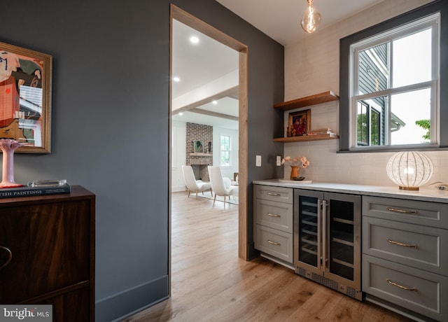 bar with beverage cooler, light wood-type flooring, backsplash, and gray cabinetry