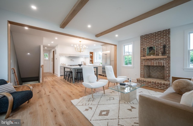 living room featuring a fireplace, light wood-type flooring, beam ceiling, and a chandelier