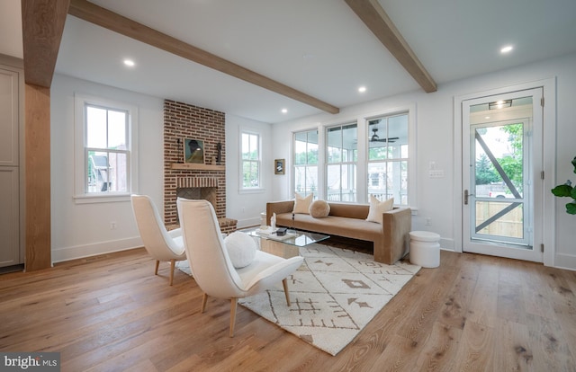 living room featuring light wood-type flooring, beam ceiling, and a fireplace