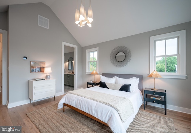 bedroom featuring wood-type flooring, an inviting chandelier, ensuite bathroom, and high vaulted ceiling