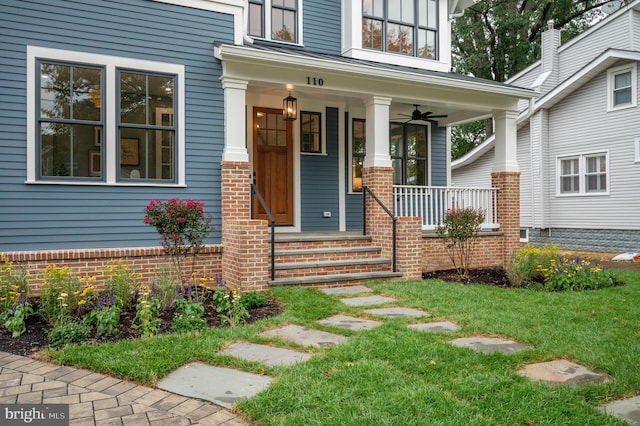 view of exterior entry featuring ceiling fan, a yard, and covered porch