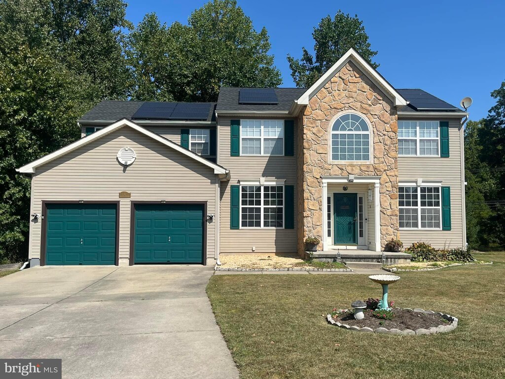 colonial home with stone siding, an attached garage, concrete driveway, solar panels, and a front lawn