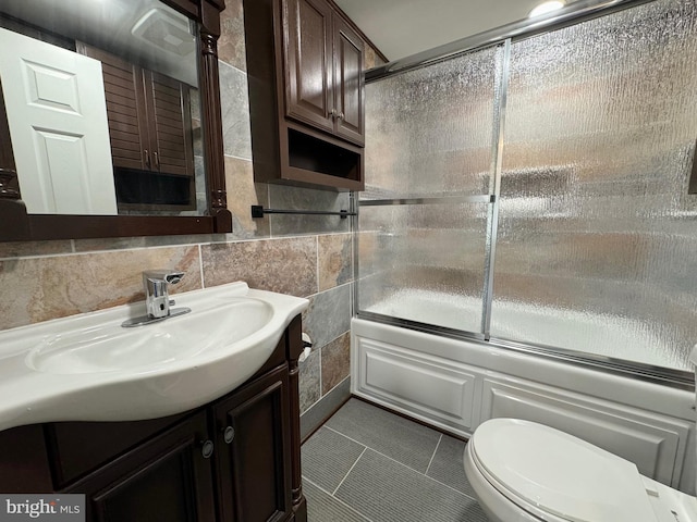 full bathroom featuring vanity, bath / shower combo with glass door, tasteful backsplash, tile walls, and toilet